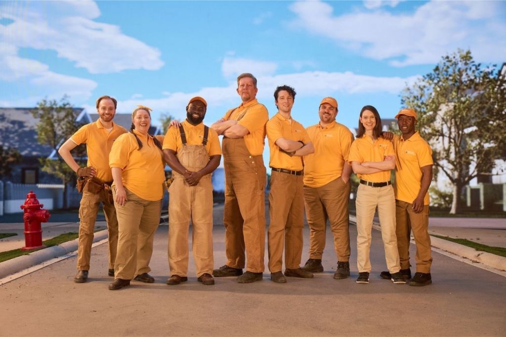 A team of home remodelers pose and smile for the camera on an empty street.