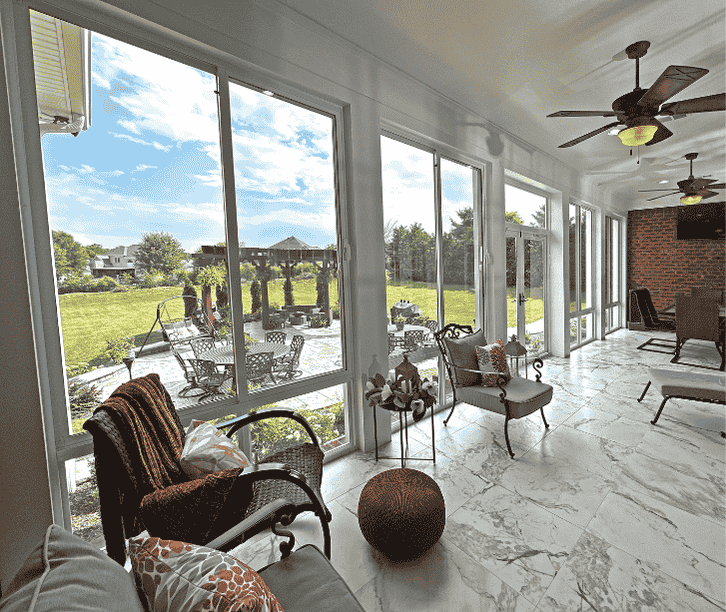 Interior of a three season sunroom enclosure with large sliding windows, tile flooring, and patio views.
