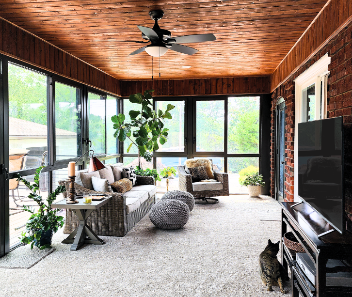 Interior view of a four season sunroom with wood plank ceiling, comfortable seating, and large windows overlooking the backyard.