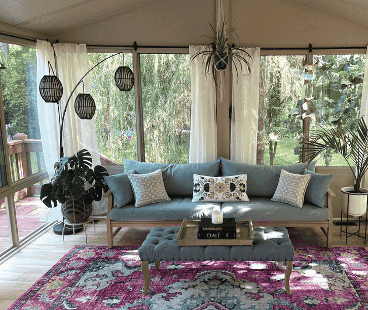 Comfortable three season sunroom interior with sofa seating, decorative lighting, and large windows overlooking greenery.