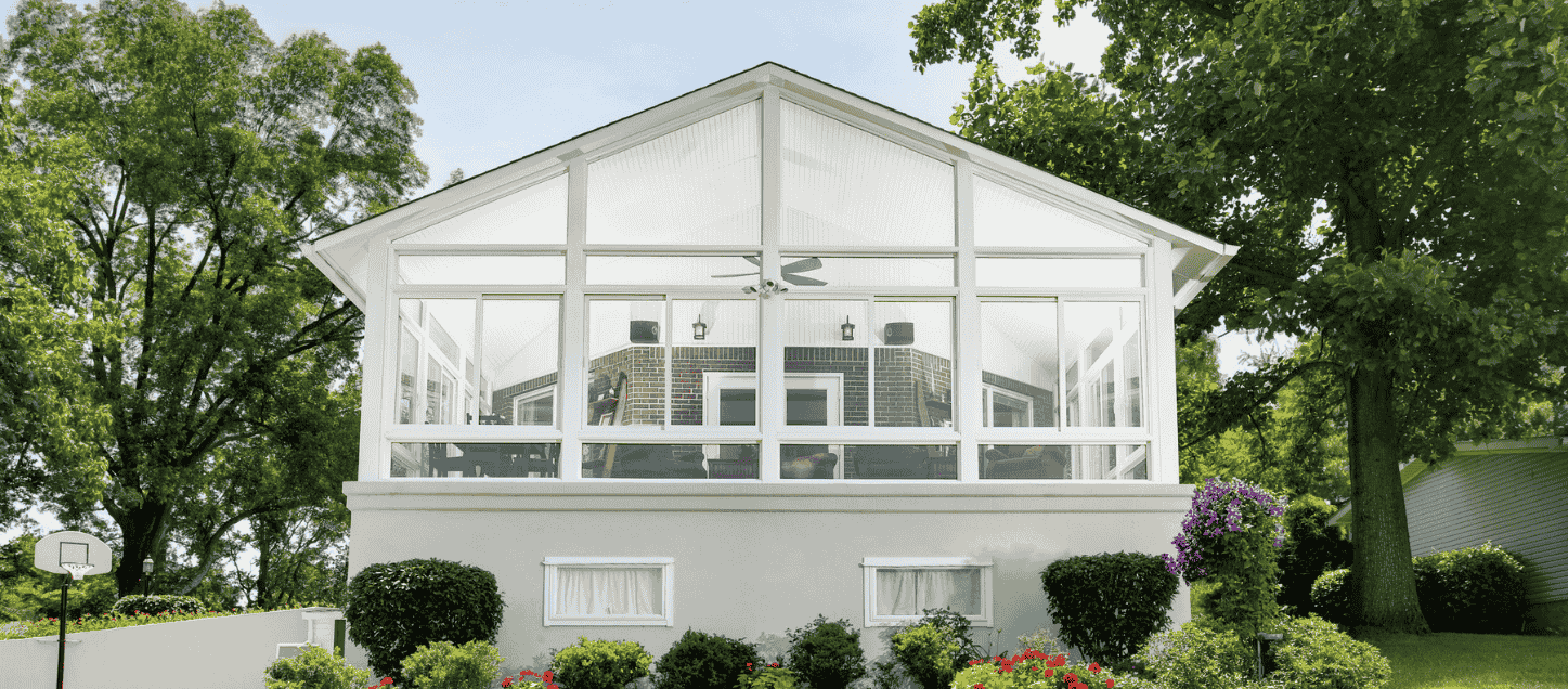 A white and bright sunroom with full views of a backyard with established trees.