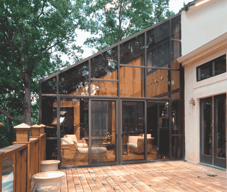 Modern solarium sunroom enclosure with floor-to-ceiling glass walls and dark framing connected to a backyard deck.