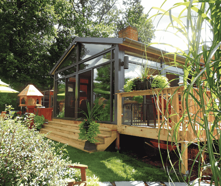 Contemporary four season sunroom with black framed glass walls, attached wooden deck, and surrounding garden landscaping.