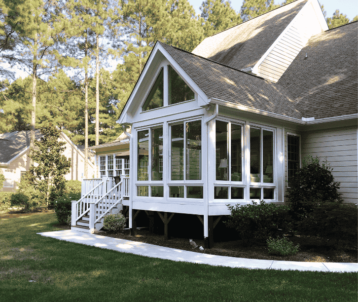 Elevated four season sunroom with tall triangular windows and white framing attached to a suburban home.