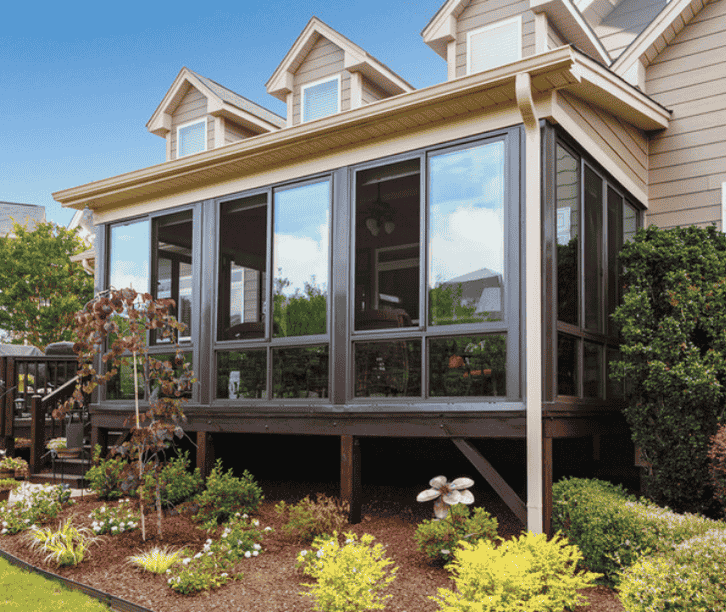Raised three season sunroom enclosure with screened windows and dark frames built onto a backyard deck.