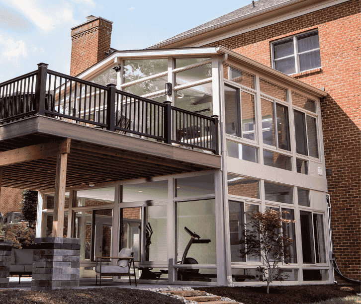 Two story four season sunroom with large glass panels built beneath a deck on a brick home.