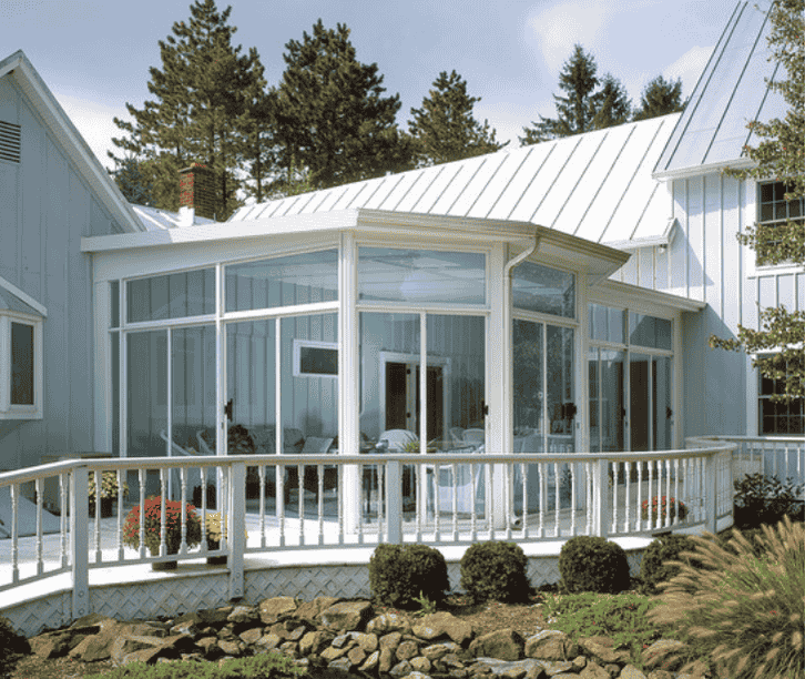 White three season sunroom enclosure with glass walls and railing overlooking landscaped yard and stone garden.