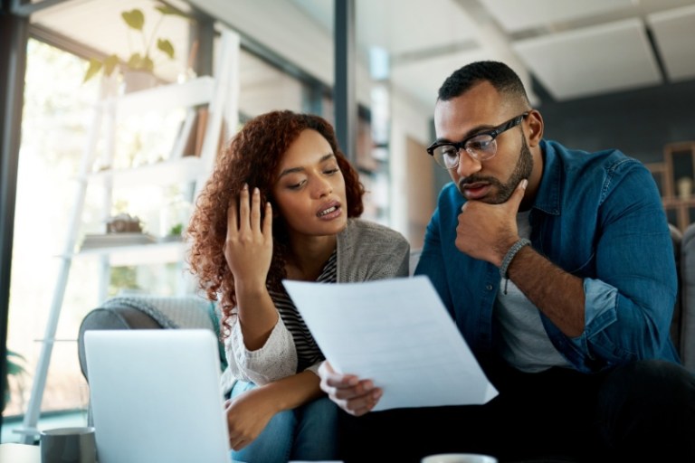 A couple sits next to each other at home, holding paperwork, and having a difficult discussion.