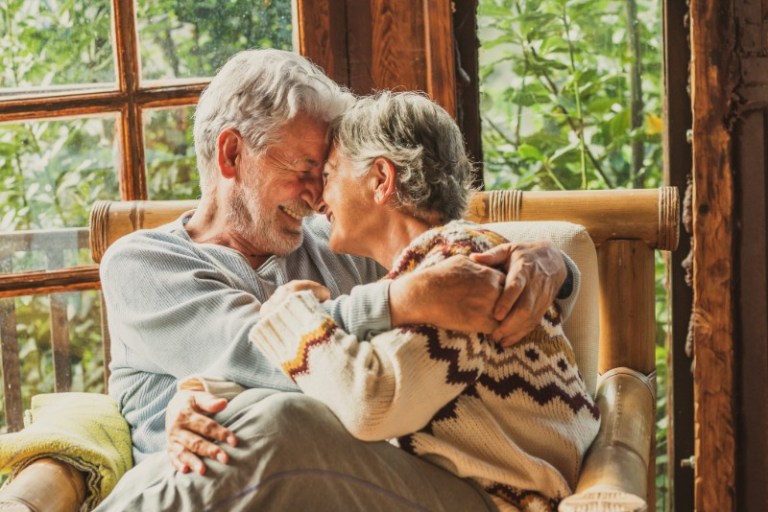An older couple smiles into each others' eyes while embracing on a large chair.