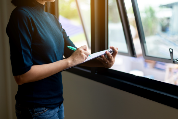 A woman inspects her new windows while making a note on paper.