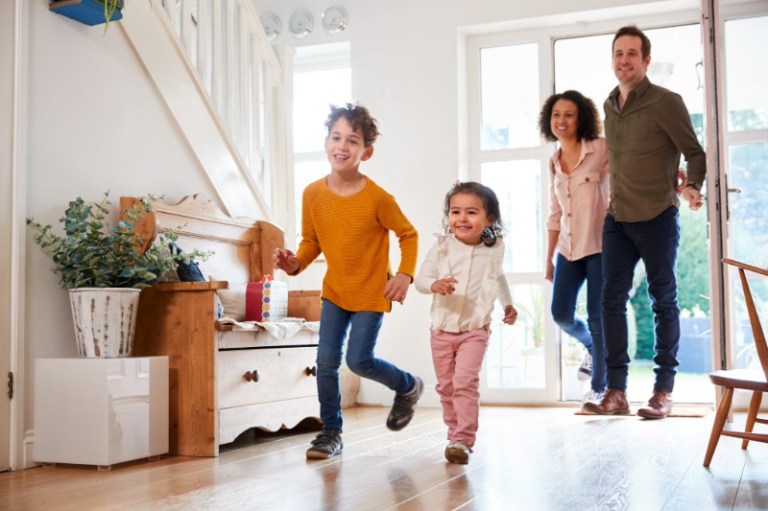 A happy family of four bursts through their front door, excited to be home.