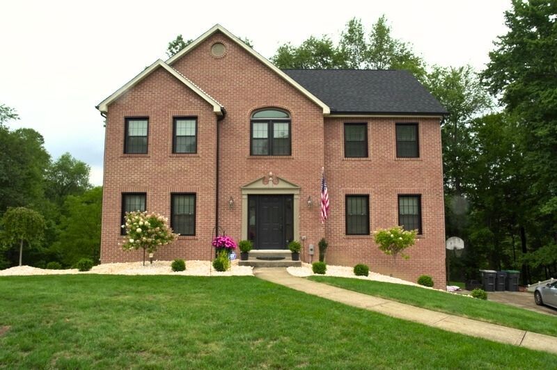 Two-story brick Colonial style home with black shutters, central front entry, gable roof, and landscaped front yard.