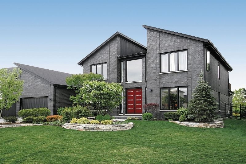 Contemporary style house with dark brick exterior, large windows, asymmetrical rooflines, and bold red front door.
