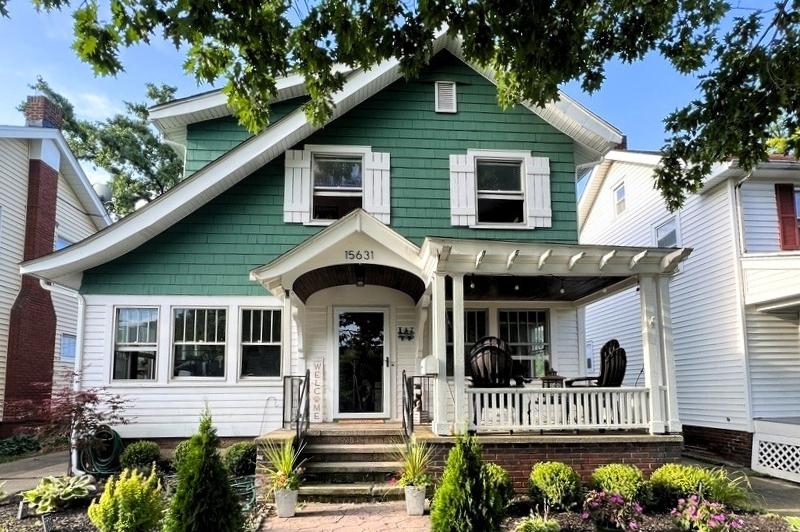 Classic Craftsman style house with green siding, white trim, front porch, exposed rafters, and landscaped yard.