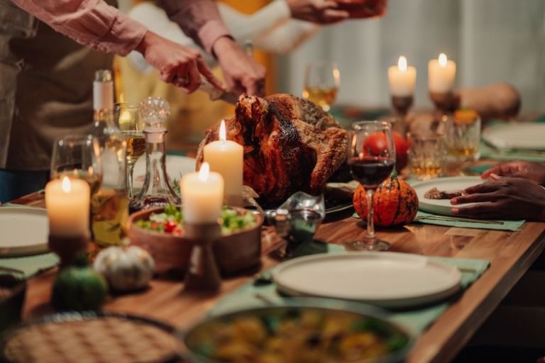 A close up of a cozy Thanksgiving table full of food, candles, and festive decor.