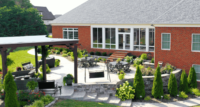 An aerial view of a brick home's 3-season room overlooking a backyard with detailed landscaping and a covered patio.