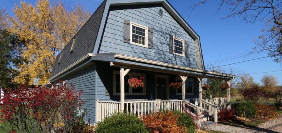 Blue farmhouse-style home with covered front porch, updated siding, and custom windows, thoughtfully remodeled by Great Day Improvements to enhance curb appeal and long-term durability.