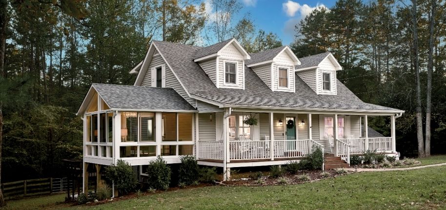 Farmhouse-style home with wraparound porch and enclosed living space, remodeled by Great Day Improvements to create inviting outdoor areas designed around the homeowner’s lifestyle.
