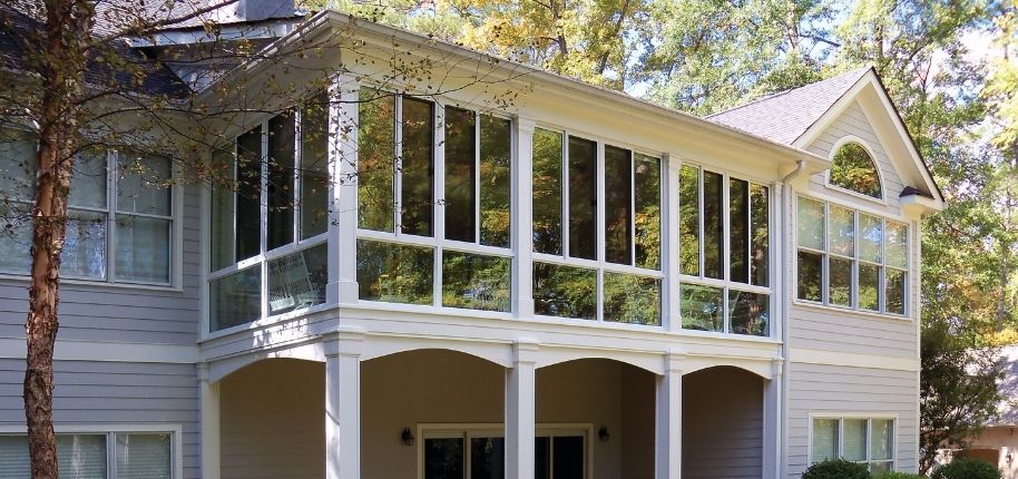 Two-story home with a full-length enclosed porch and expansive windows, remodeled by Great Day Improvements to add bright, comfortable living space with outdoor views.