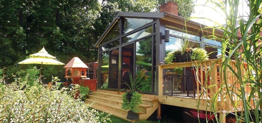 Backyard view of a home with a custom glass sunroom and wood deck, remodeled by Great Day Improvements to create a seamless indoor-outdoor living retreat.