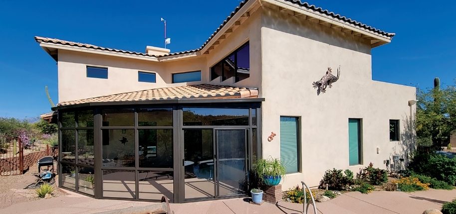 Southwest-style stucco home with a custom screened sunroom addition and expansive glass panels, remodeled by Great Day Improvements to enhance indoor-outdoor living and comfort.