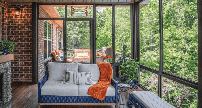 The interior of a window-walled sunroom with a view of a back deck and enclosed by trees.