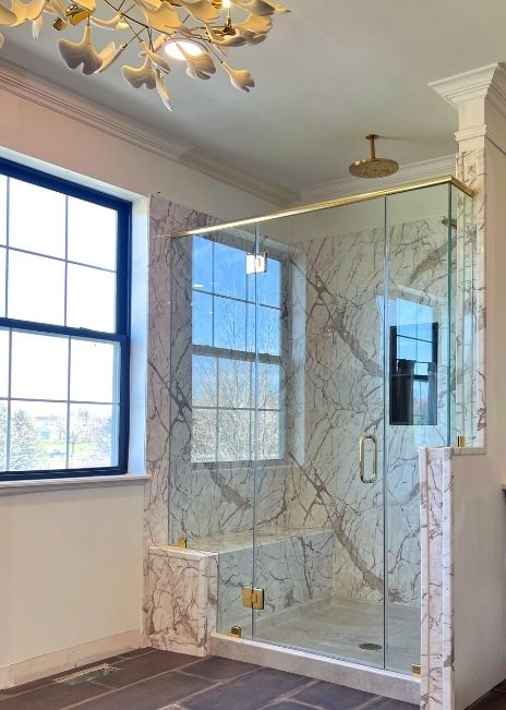 A white marble shower with glass door in an open and airy bathroom.
