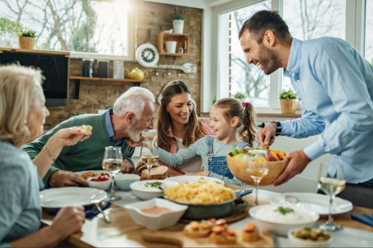 Multi-generational family happily gathers around a dining table for a meal at home.
