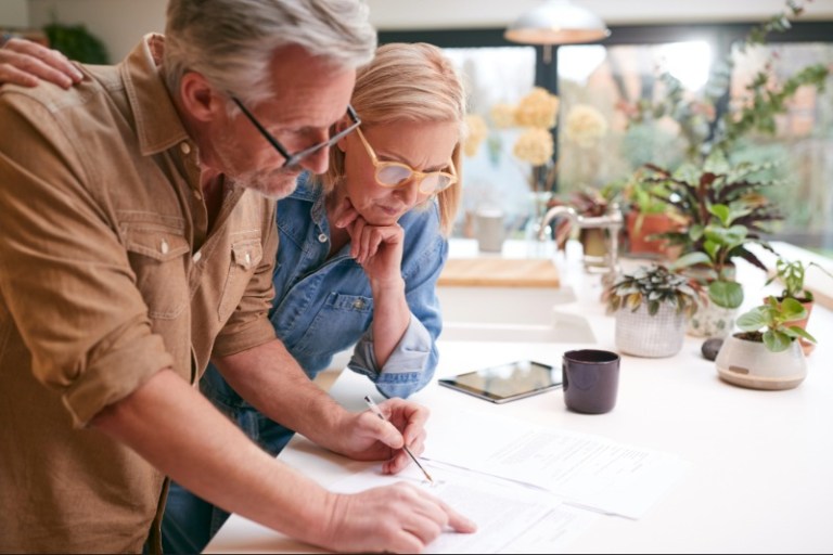 A mature couple carefully reviews some paperwork at their bright and airy kitchen counter.