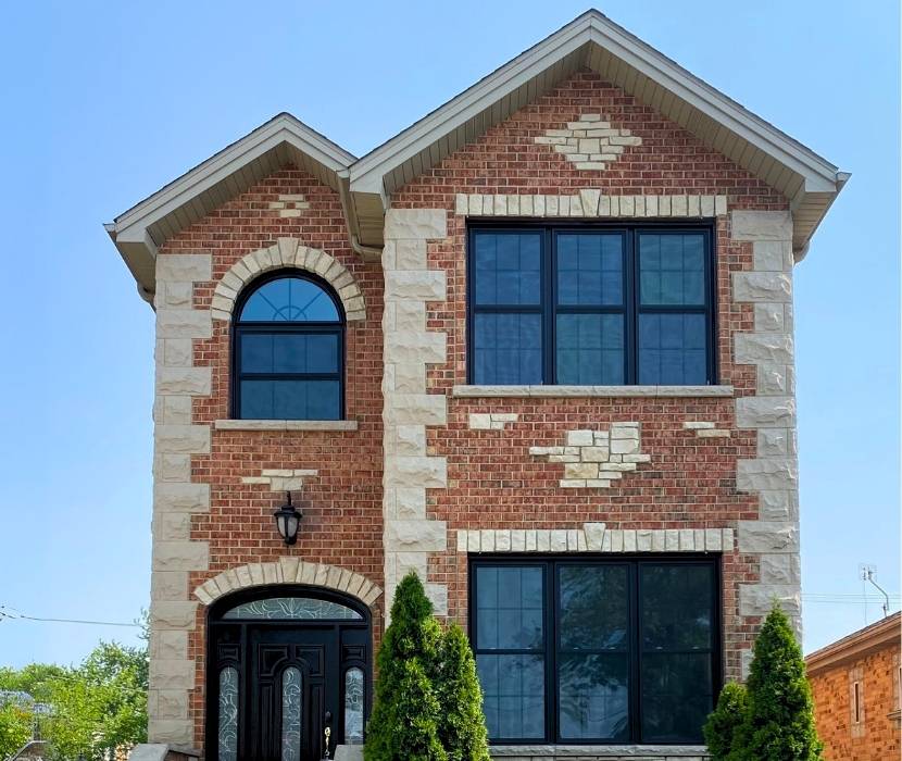 A modern brick home featuring newly installed black frame windows on both floors, showcasing professional window replacement service by Great Day Improvements.