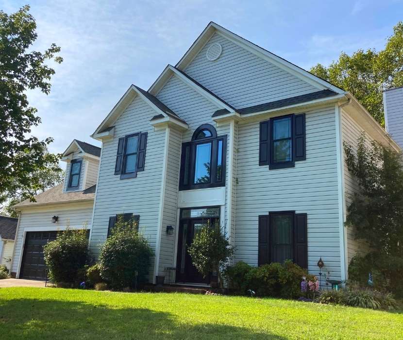 White colonial-style home featuring new black-trim windows and a large arched window over the front entryway, expertly installed by Great Day Improvements.
