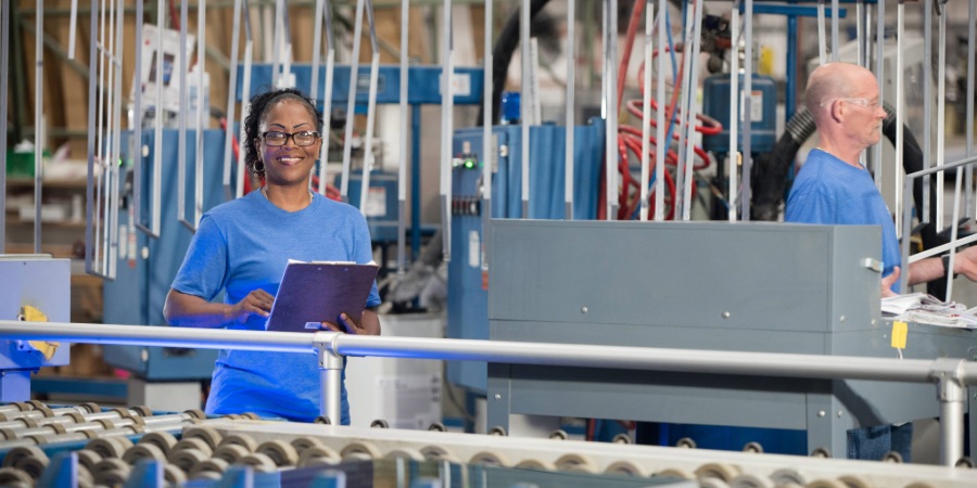 A woman proudly stands with a clipboard in a Great Day Improvements window factory.