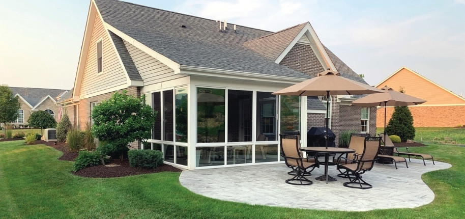 Brick home with white sunroom addition and stamped concrete patio, renovated by Great Day Improvements to expand bright, functional living space.