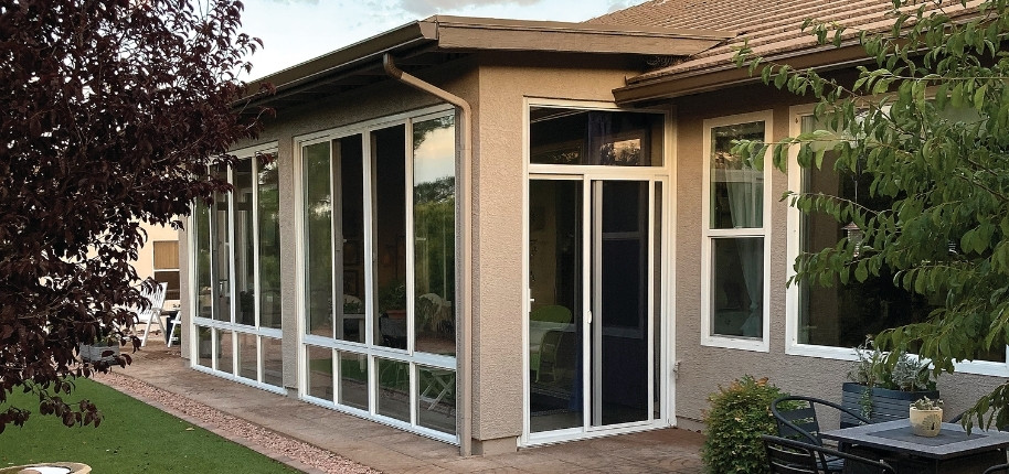 Stucco home with glass sunroom addition and sliding patio doors, renovated by Great Day Improvements to create a bright, climate-controlled living space.