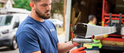 An installer extrudes a custom Leafguard gutter on a job site.