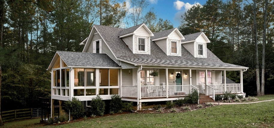 Farmhouse-style home with wraparound porch and glass sunroom addition, renovated by Great Day Improvements for year-round comfort and expanded living space.