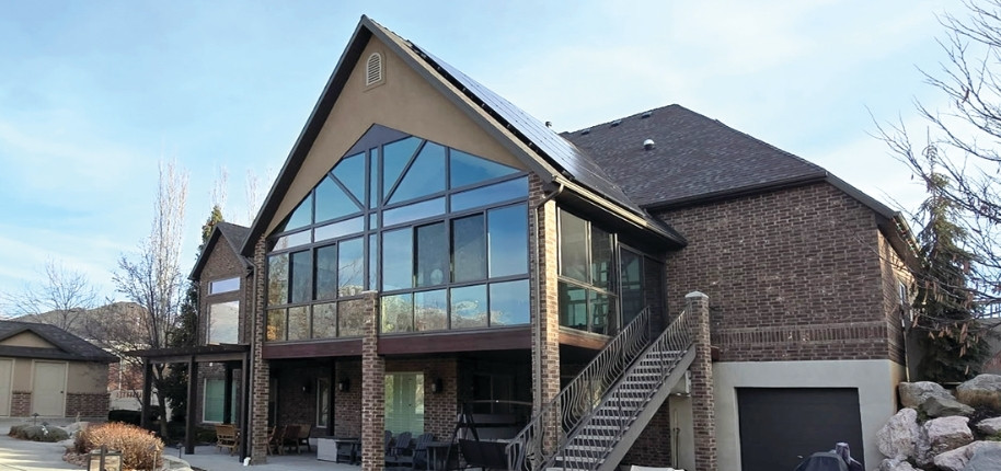 Brick home with dramatic two-story glass sunroom addition and elevated deck, renovated by Great Day Improvements to expand living space and maximize natural light.