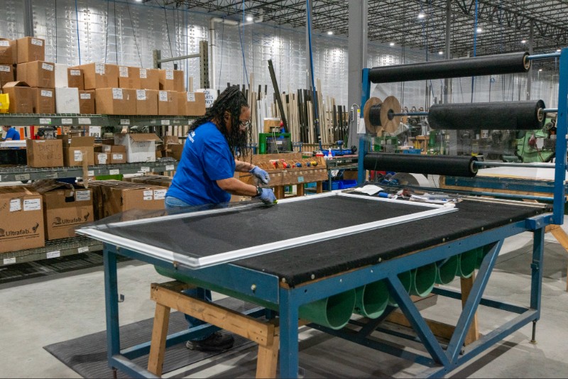 A worker at Great Day Improvements manufacturing facility installs a screen into a door.