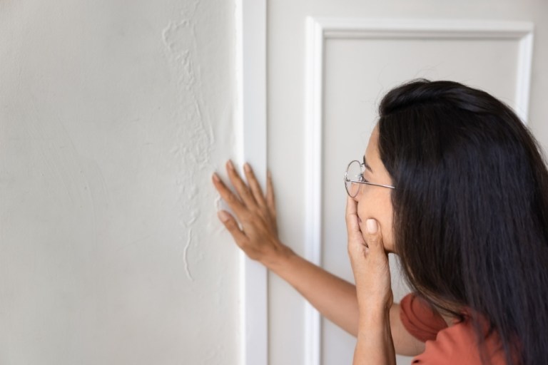 A concerned woman inspects water damage to the wall of her house.